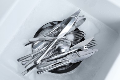 Washing silver spoons, forks and knives in kitchen sink with foam, flat lay