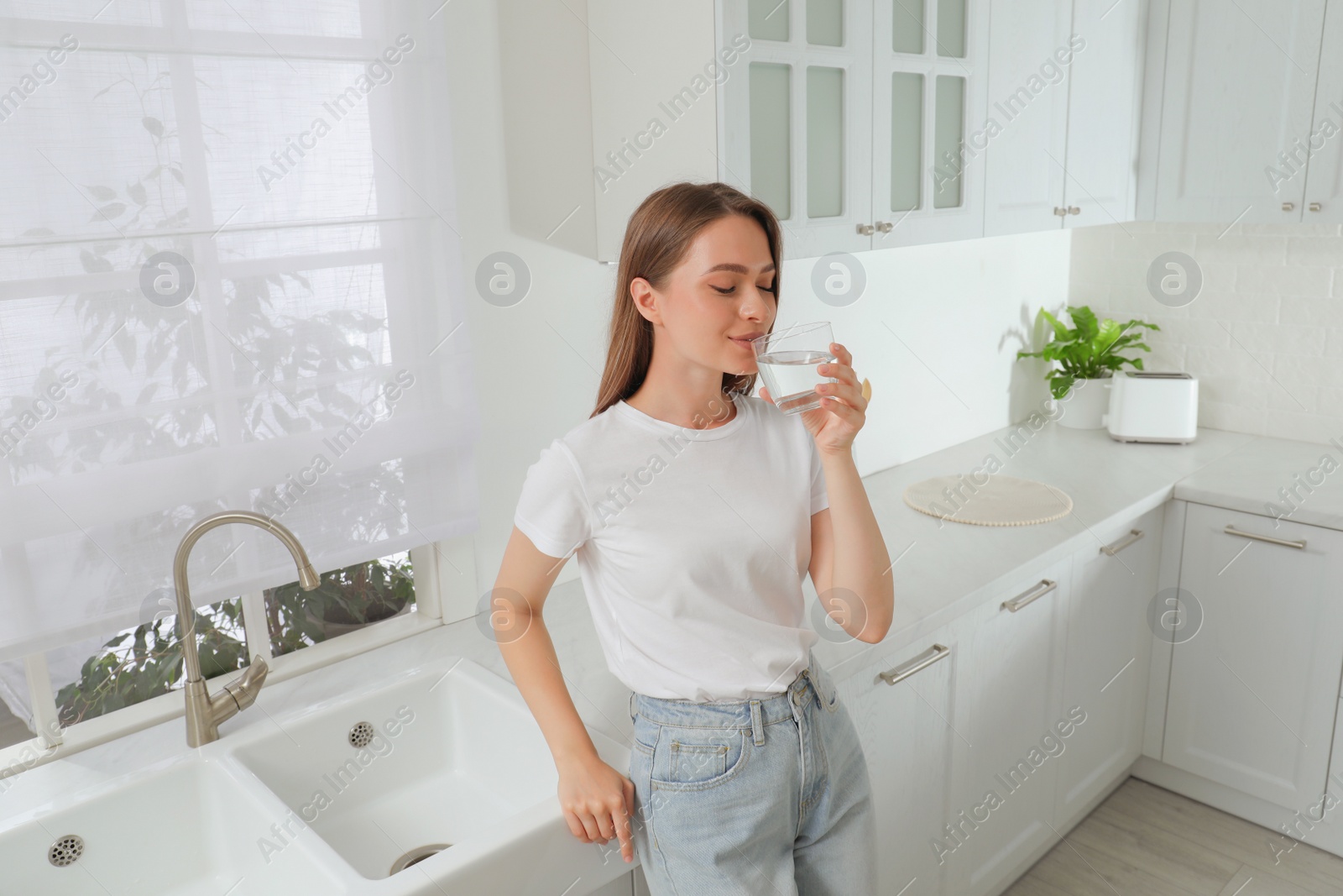 Photo of Woman drinking tap water from glass in kitchen