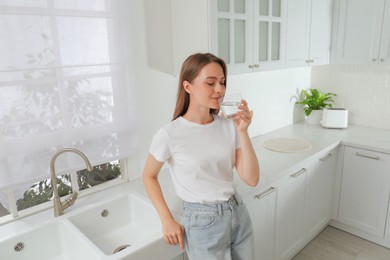 Photo of Woman drinking tap water from glass in kitchen