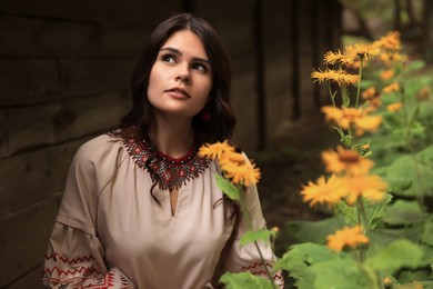 Beautiful woman wearing embroidered dress in blooming garden. Ukrainian national clothes