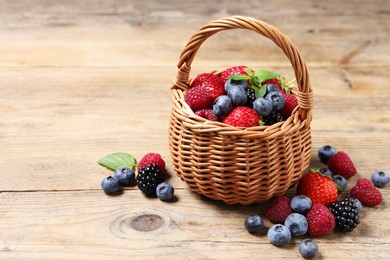 Photo of Wicker basket with many different fresh ripe berries on wooden table, space for text