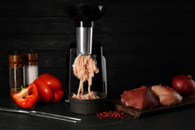 Photo of Electric meat grinder with chicken mince and products on black table