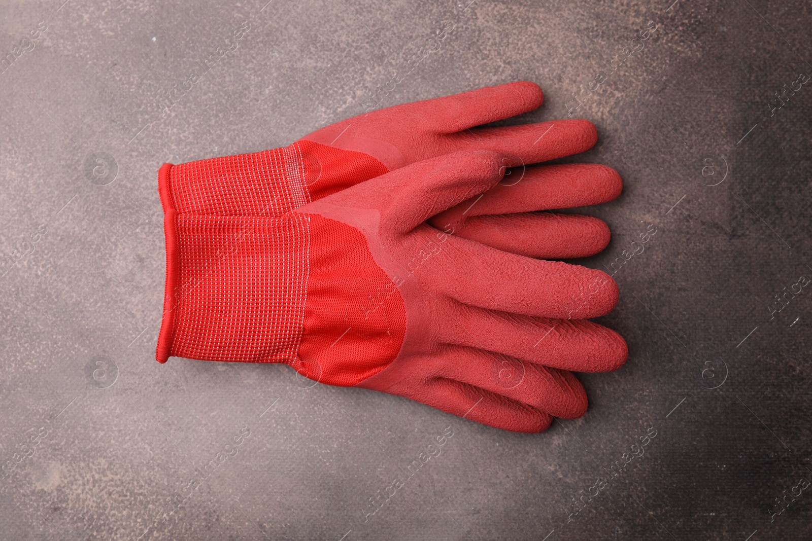 Photo of Pair of red gardening gloves on brown textured table, top view