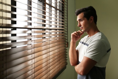 Handsome young man looking out window indoors