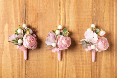 Photo of Stylish pink boutonnieres on wooden table, flat lay