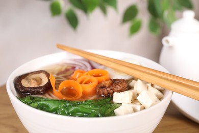Photo of Delicious vegetarian ramen with mushrooms, tofu, vegetables and chopsticks on table, closeup