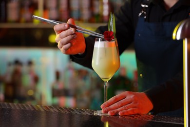 Photo of Bartender decorating fresh alcoholic cocktail with flower at bar counter, closeup. Space for text