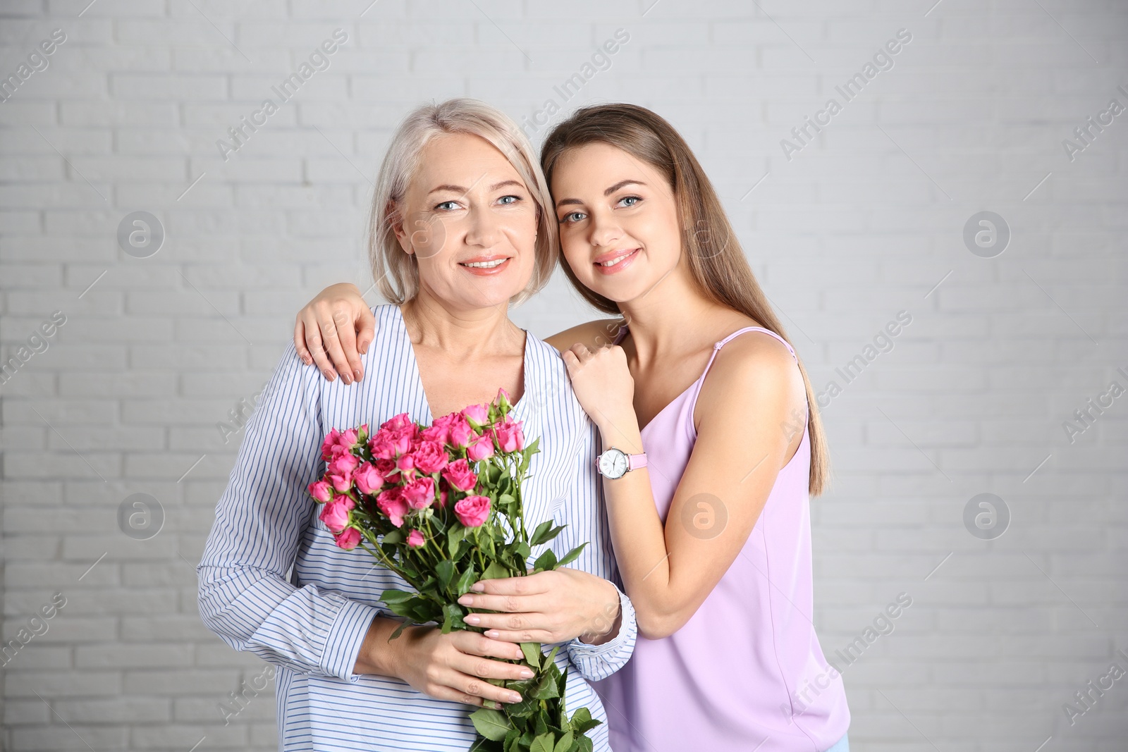 Photo of Young daughter congratulating her mature mother near brick wall. Happy Women's Day