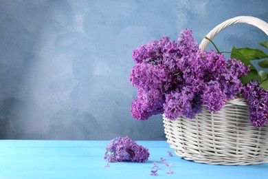 Photo of Beautiful lilac flowers in wicker basket on light blue wooden table, space for text