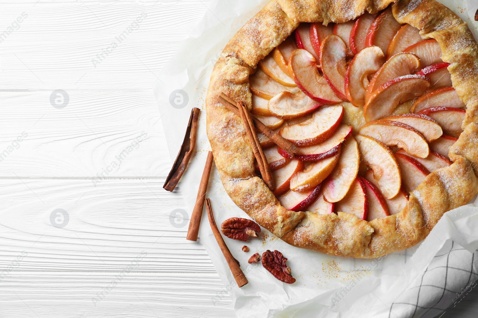 Photo of Delicious apple galette, cinnamon and pecans on white wooden table, flat lay. Space for text