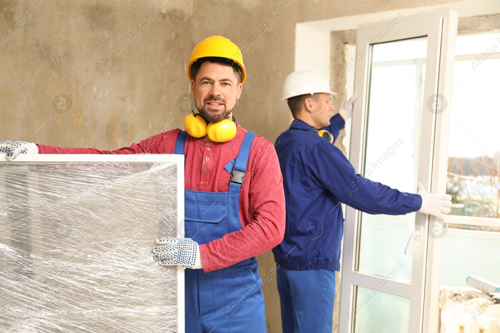 Photo of Workers in uniform installing plastic windows indoors