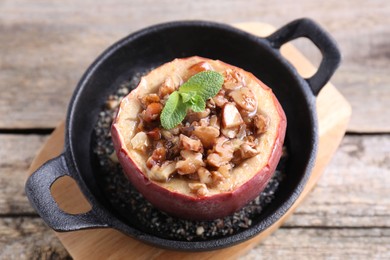 Photo of Tasty baked apple with nuts, honey and mint in baking dish on wooden table, above view