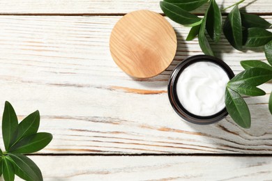 Photo of Jar of face cream and green leaves on wooden table, flat lay. Space for text