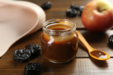 Photo of Tasty baby food in jar, spoon and dried prunes on wooden table, closeup