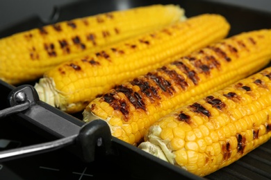 Photo of Grill pan with tasty fresh corn cobs on stove, closeup