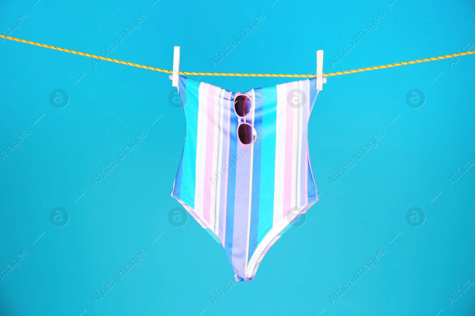 Photo of Beautiful swimsuit and sunglasses hanging on rope against color background