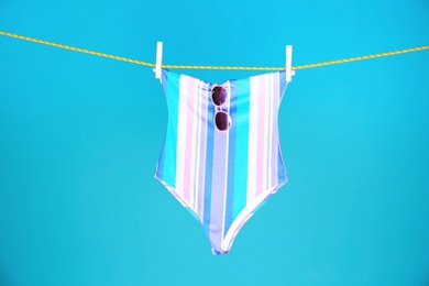 Beautiful swimsuit and sunglasses hanging on rope against color background