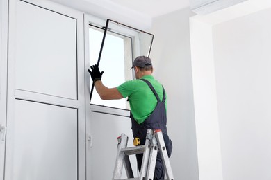 Worker on folding ladder installing window indoors