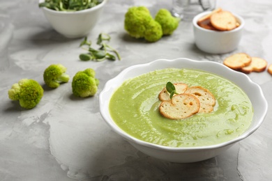 Photo of Bowl of broccoli cream soup with croutons served on grey table