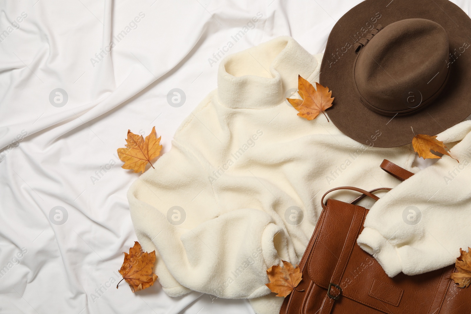 Photo of Flat lay composition with warm sweater and dry leaves on white fabric. Autumn season