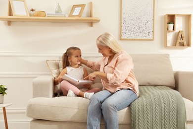 Photo of Happy grandmother with her granddaughter reading book together at home