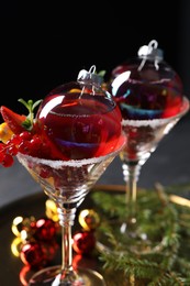 Photo of Creative presentation of Christmas Sangria cocktail in baubles and glasses on table against black background, closeup
