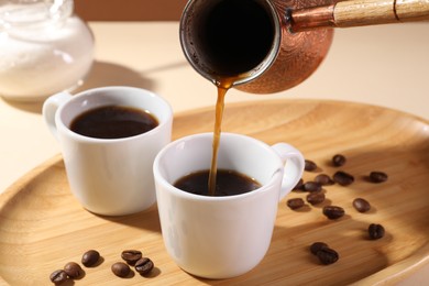 Pouring aromatic coffee from cezve into cup at table, closeup