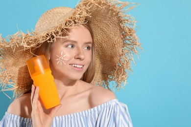 Photo of Beautiful young woman in straw hat with sun protection cream on light blue background