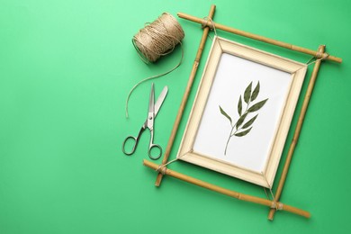 Photo of Bamboo frame with dried plant, scissors and twine on green background, flat lay. Space for text