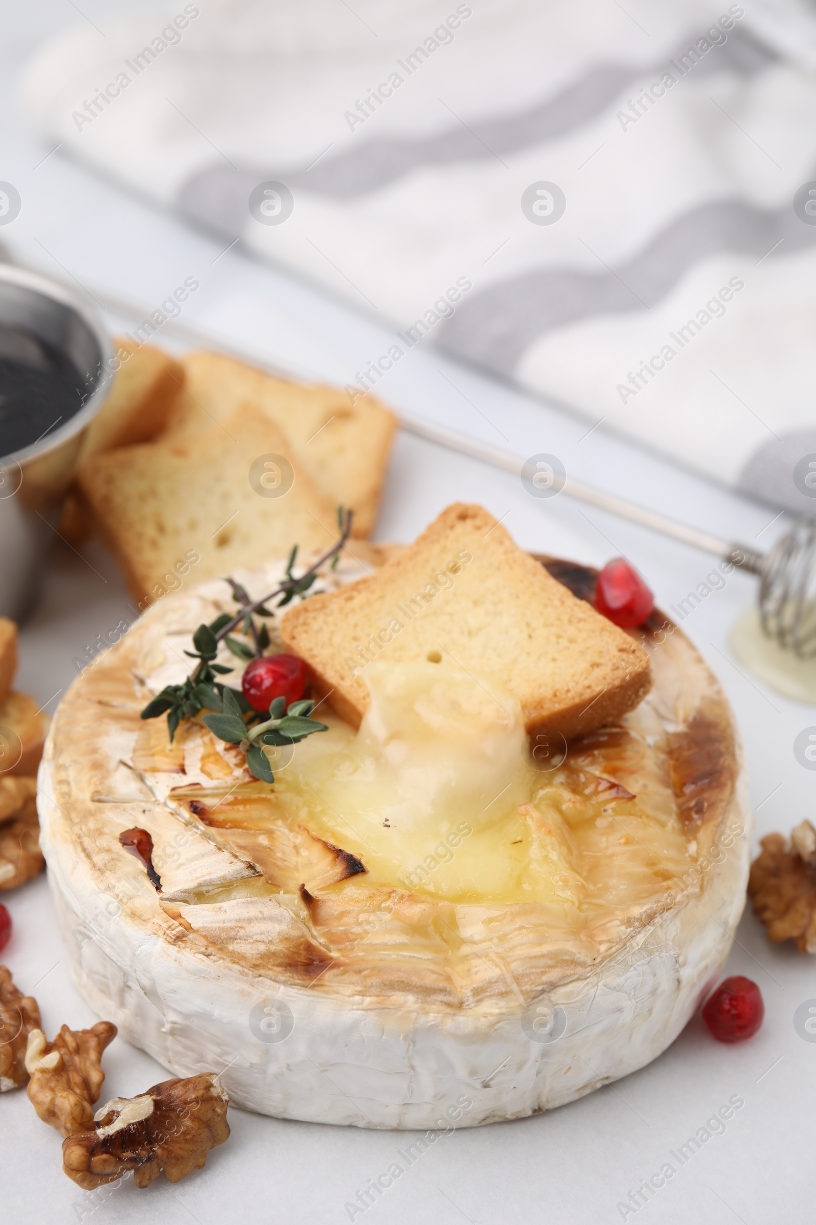 Photo of Tasty baked camembert with crouton, thyme, walnuts and pomegranate seeds on white table, closeup