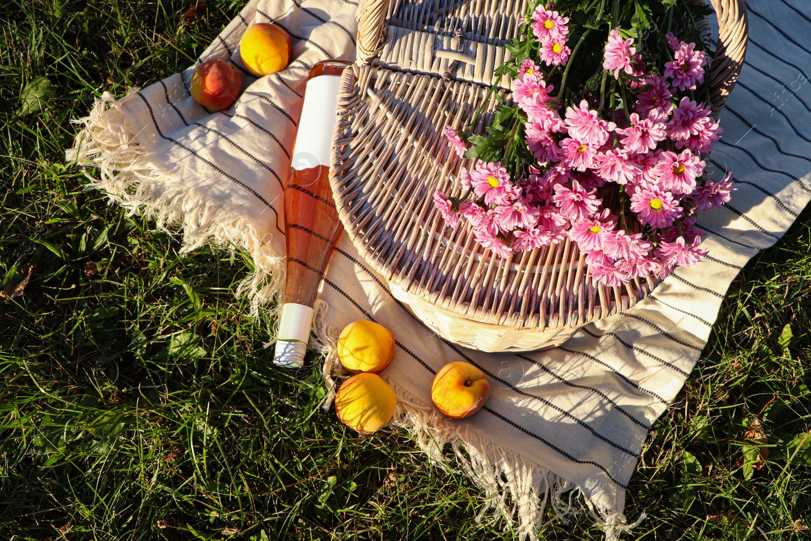 Photo of Picnic basket, flowers, peaches and bottle of wine on blanket outdoors, top view