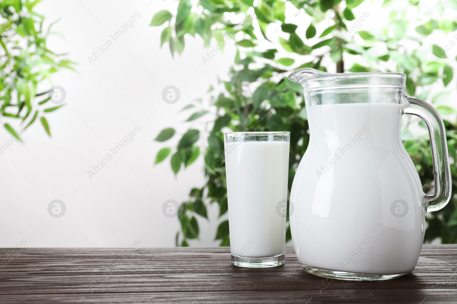 Photo of Jug and glass with fresh milk on wooden table against blurred background. Space for text