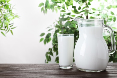 Jug and glass with fresh milk on wooden table against blurred background. Space for text