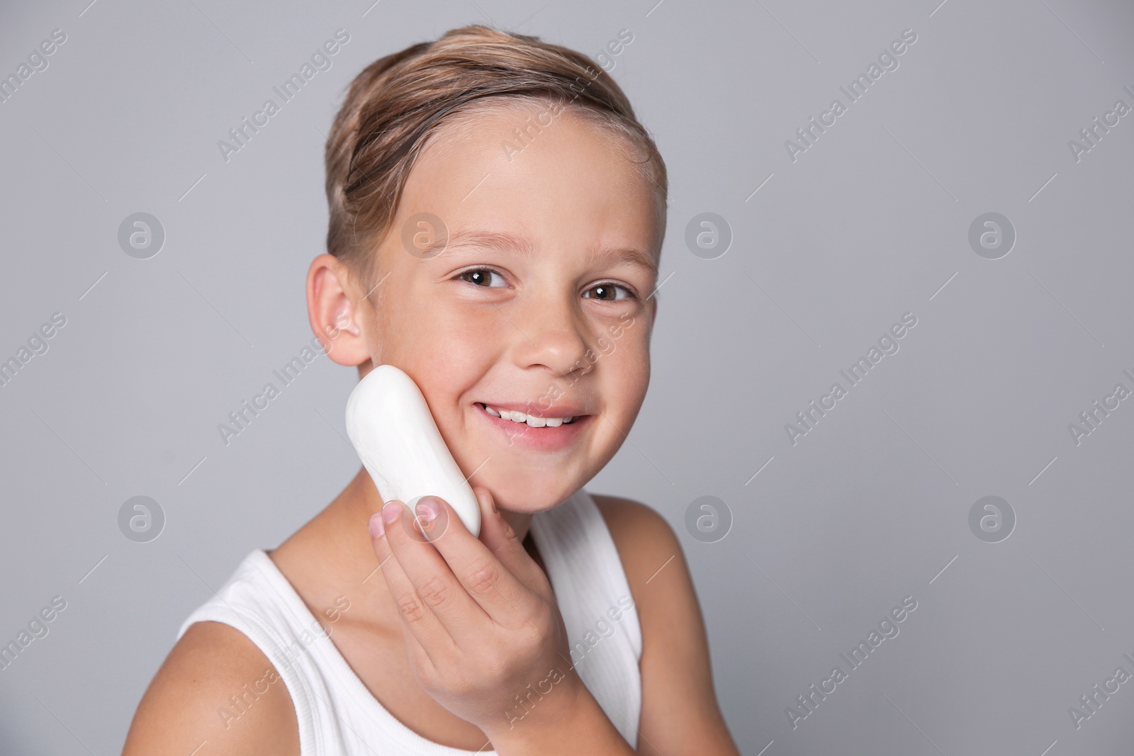 Photo of Cute little boy with soap bar on gray background