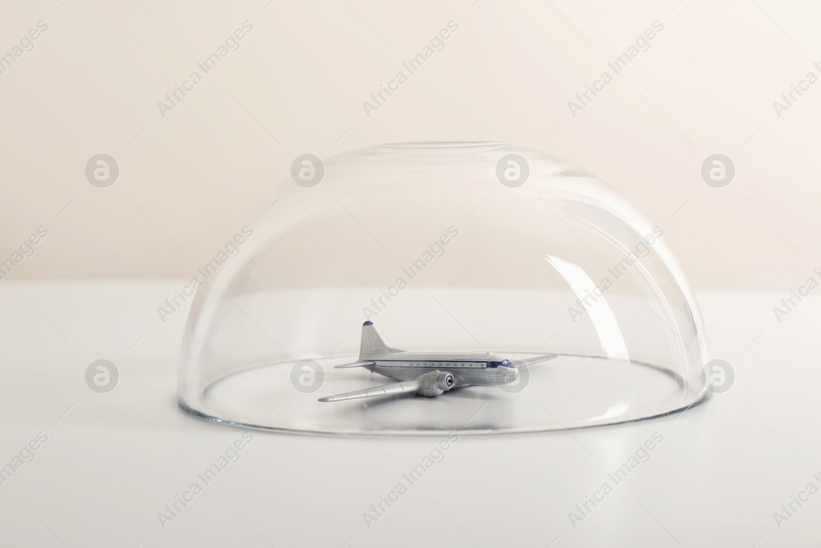 Photo of Toy plane under glass dome on white table. Travel insurance concept
