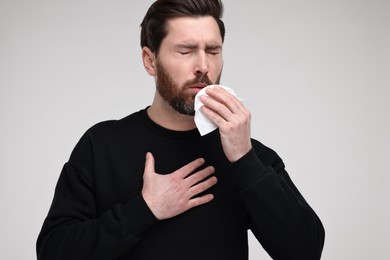 Sick man with tissue coughing on light grey background