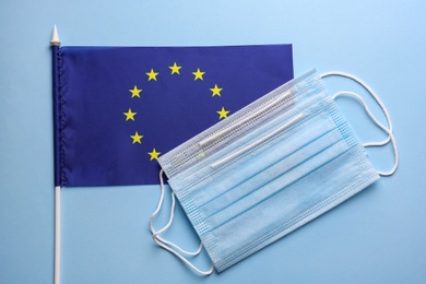 Photo of European Union flag and protective masks on light blue background, flat lay. Coronavirus outbreak