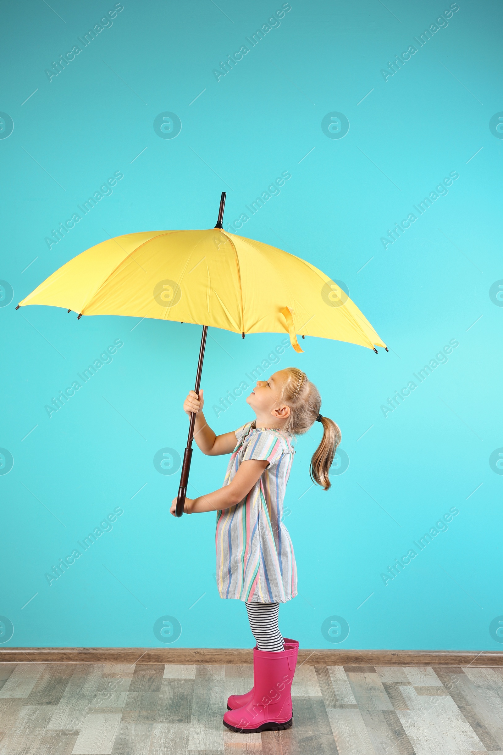 Photo of Little girl with yellow umbrella near color wall