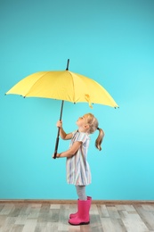 Little girl with yellow umbrella near color wall