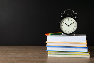 Photo of Alarm clock and stacked books on wooden table near blackboard, space for text. School time