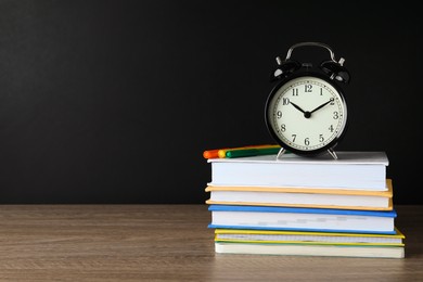 Alarm clock and stacked books on wooden table near blackboard, space for text. School time