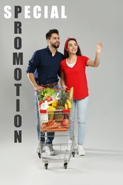 Image of Special promotion. Young couple with shopping cart fullgroceries on grey background