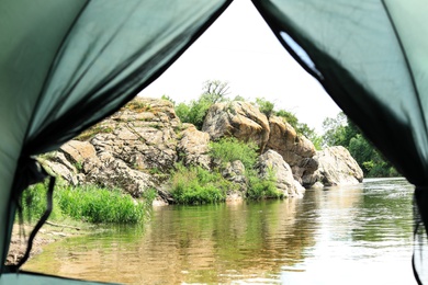 Calm river with rocky bank, view from camping tent