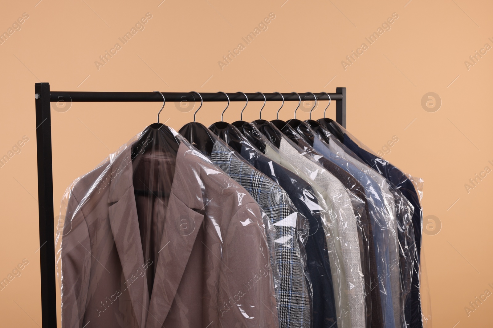 Photo of Dry-cleaning service. Many different clothes in plastic bags hanging on rack against beige background