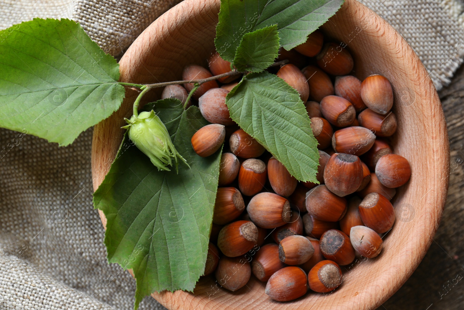 Photo of Tasty hazelnuts and green leaves on wooden table, top view. Healthy snack