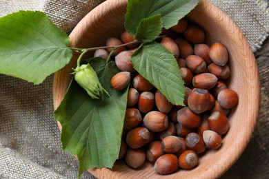 Tasty hazelnuts and green leaves on wooden table, top view. Healthy snack