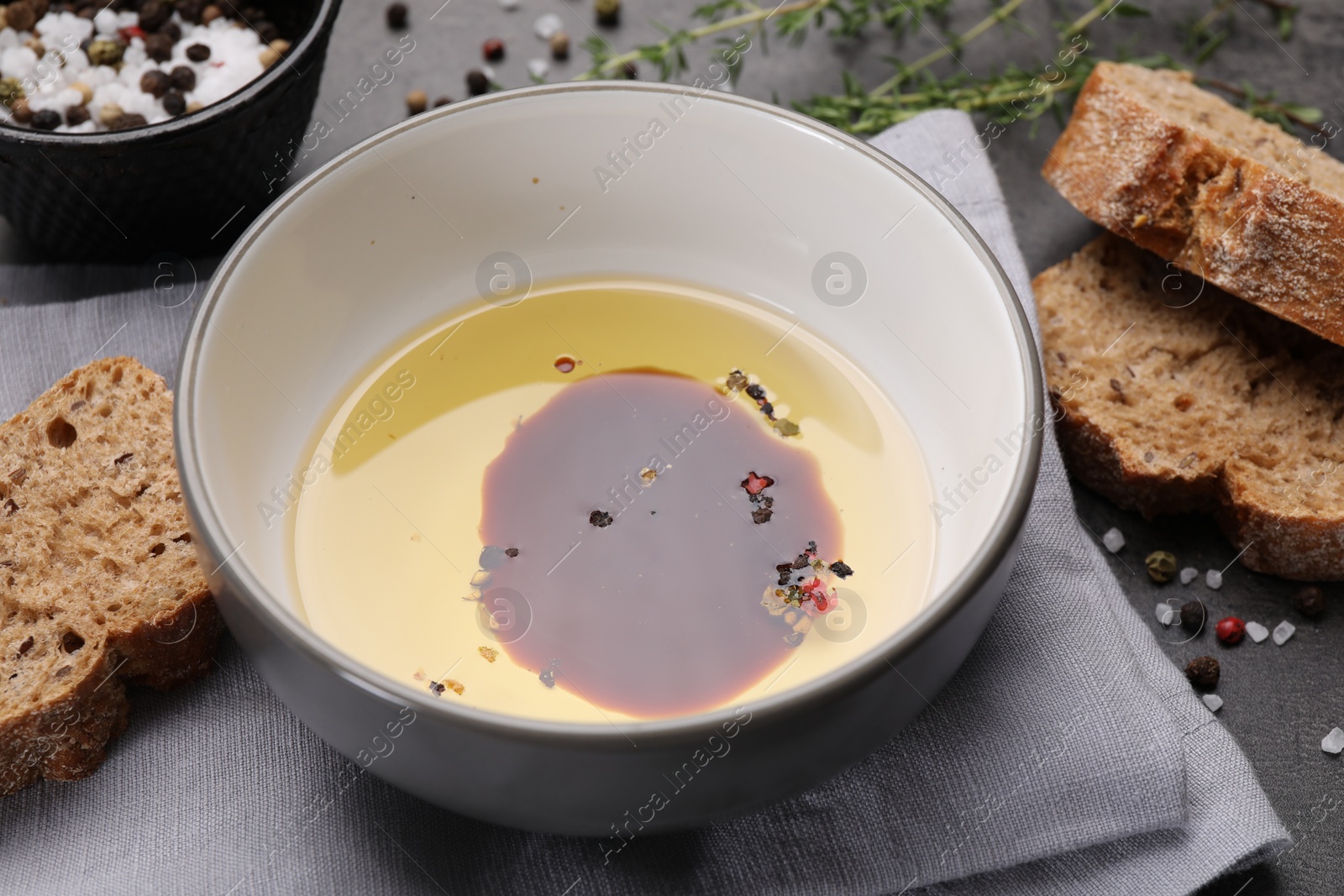 Photo of Bowl of organic balsamic vinegar with oil, spices and bread slices on grey table, closeup