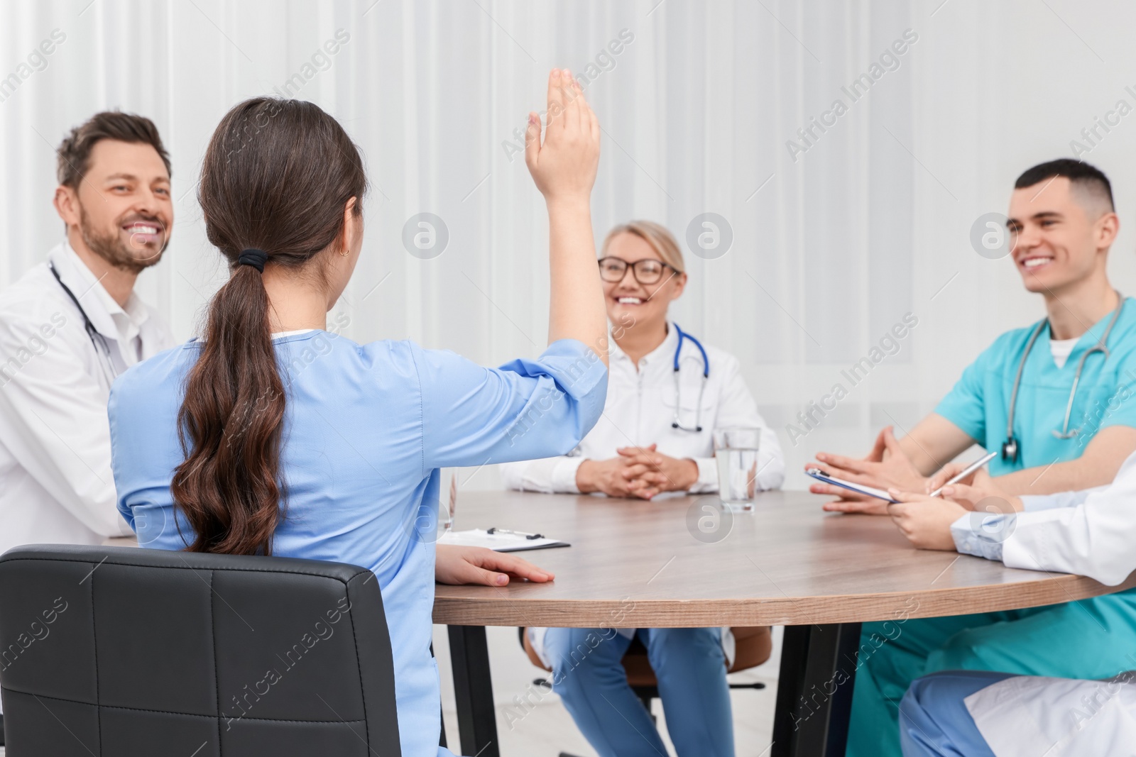 Photo of Medical conference. Team of doctors having discussion at wooden table in clinic