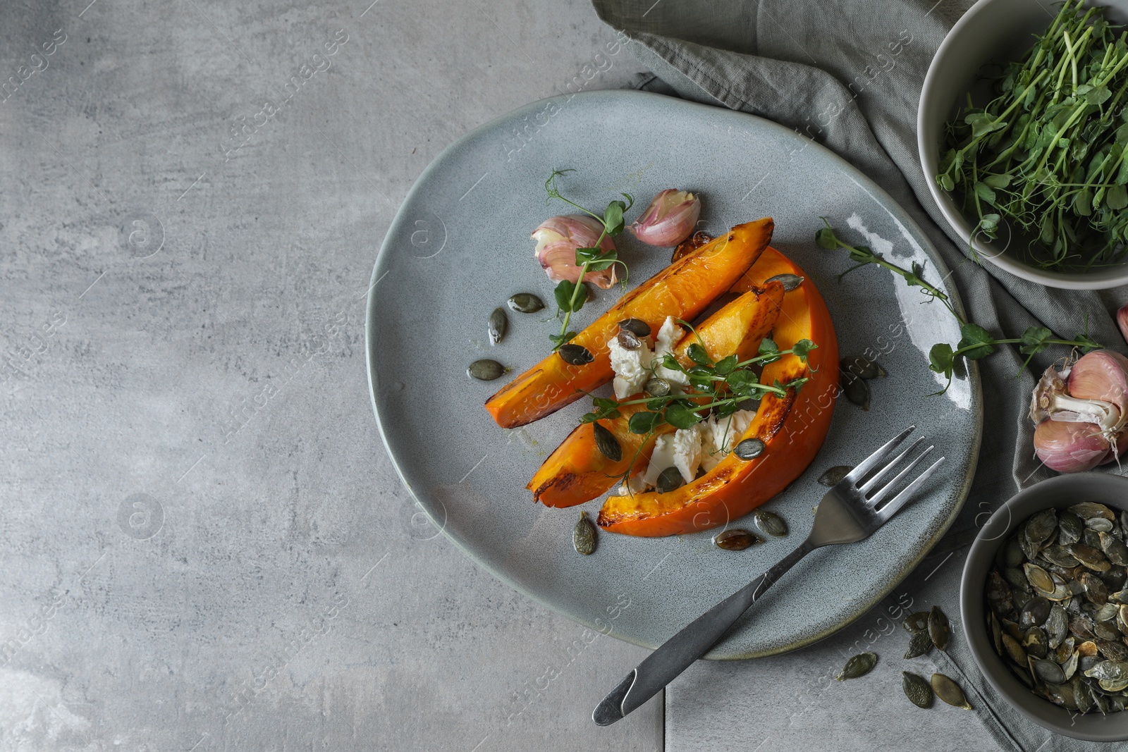 Photo of Baked pumpkin slices served with cheese, microgreens, seeds and garlic on light table, flat lay. Space for text