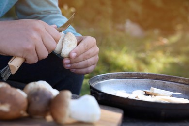 Photo of Man cutting mushroom with knife at table outdoors, closeup